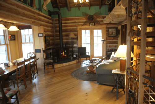 Cozy log cabin interior with a dining area, fireplace, and comfortable seating, featuring rustic decor and warm lighting.