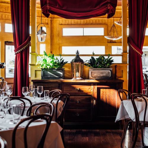 Cozy restaurant interior with wooden furniture, potted plants, and elegant table settings under warm lighting.
