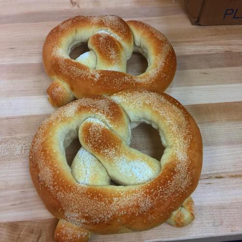 A large, soft pretzel shaped like the number 8, sprinkled with coarse salt, resting on a wooden surface.