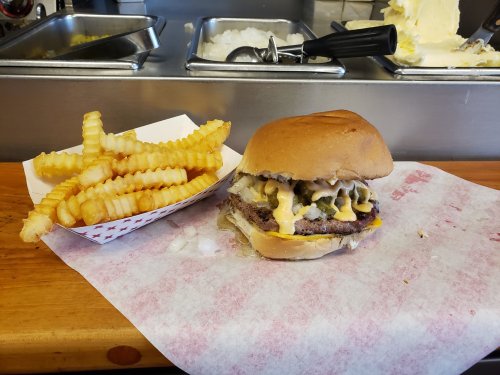 A juicy burger with cheese and toppings beside a serving of crinkle-cut fries on a wooden table.
