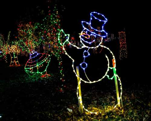 A glowing snowman made of colorful lights waves in a festive, illuminated outdoor display.