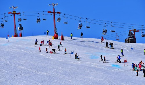 Skiers and snowboarders on a snowy slope with ski lifts in a clear blue sky.
