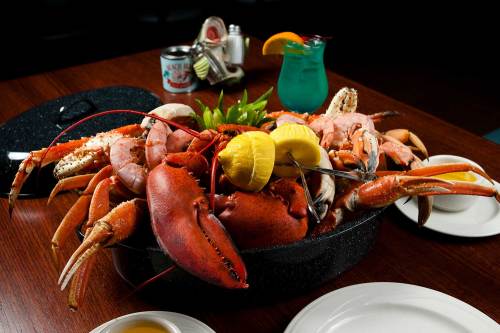 A large seafood platter featuring lobster, shrimp, and crab, garnished with lemon and served on a dark platter.