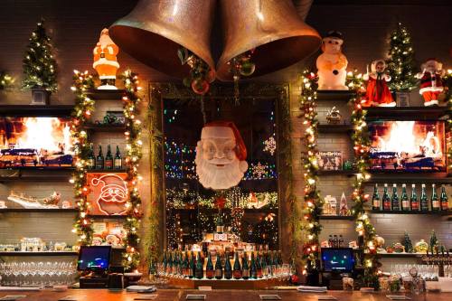 A festive bar decorated with Christmas lights, Santa figures, and a large Santa face above a mirror, creating a cozy holiday atmosphere.