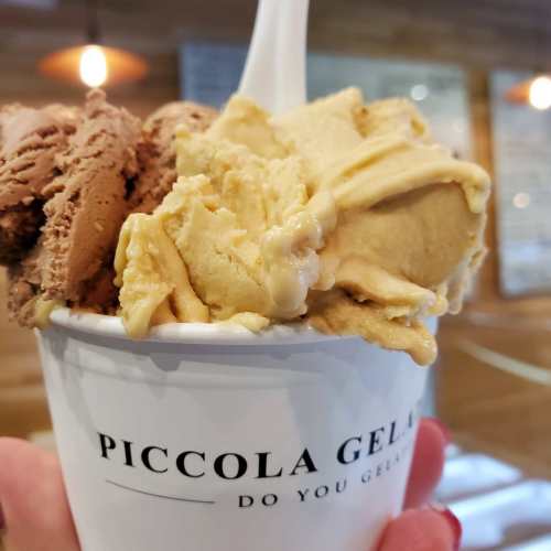 A hand holding a cup of gelato with chocolate and caramel flavors, labeled "Piccola Gelato."