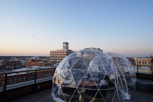 Two transparent geodesic domes on a rooftop with a city skyline at sunset in the background.