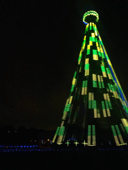 A brightly lit Christmas tree structure with green and yellow lights, set against a dark night sky.