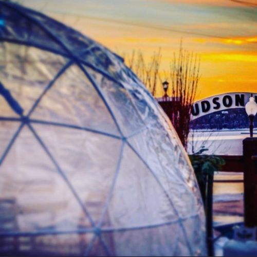 A transparent dome in the foreground with a sunset and a sign reading "HUDSON" in the background.