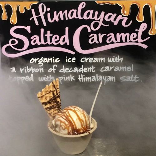 A bowl of Himalayan salted caramel ice cream topped with caramel drizzle and pink Himalayan salt, with a waffle cone.