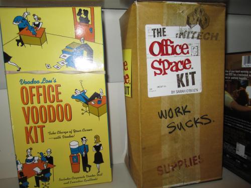 Two kits on a shelf: "Voodoo Lou's Office Voodoo Kit" and "The Office Space Kit," labeled "Work Sucks."