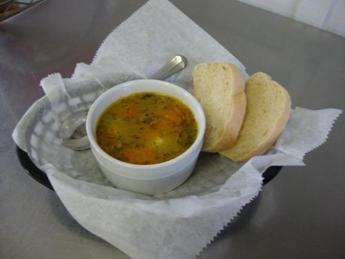 A bowl of soup with carrots and herbs, served with two slices of bread on a paper-lined plate.