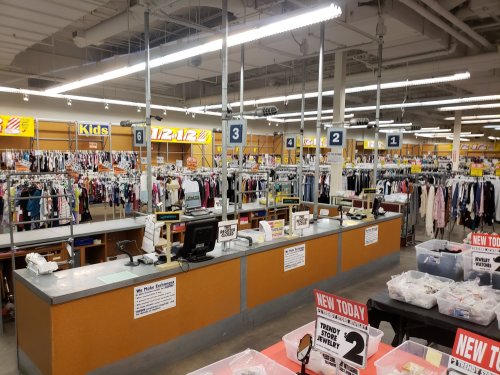 A retail store interior with clothing racks, checkout counters, and signs displaying promotions and sections for kids.