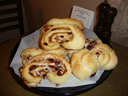 A plate of freshly baked cinnamon rolls with a swirl of icing and cranberries, served at a cozy café.