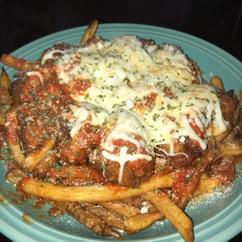 A plate of fries topped with marinara sauce, melted cheese, and herbs, creating a hearty, savory dish.
