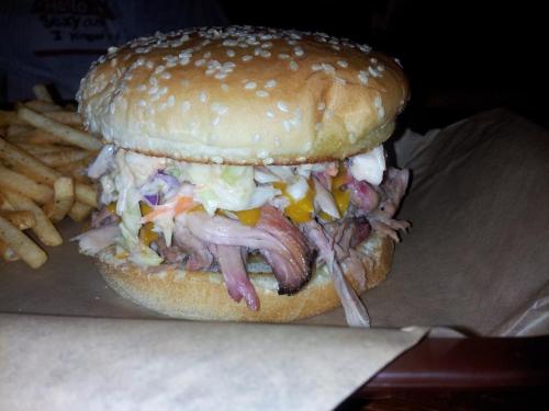 A sesame seed bun sandwich filled with pulled pork, coleslaw, and cheese, served with a side of fries.