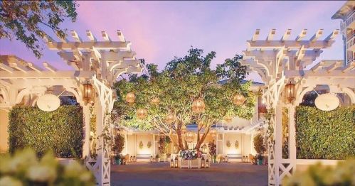 A beautifully decorated outdoor venue with white pergolas, lush greenery, and hanging lanterns at sunset.