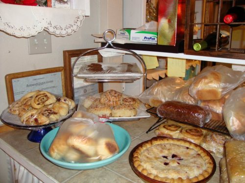 A variety of baked goods displayed on a countertop, including pastries, bread, and a pie.
