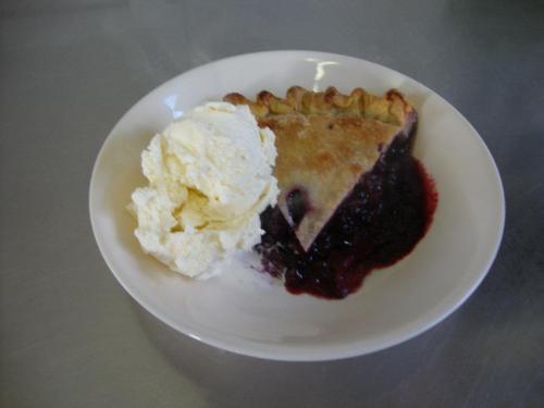 A slice of berry pie on a plate, served with a scoop of vanilla ice cream.
