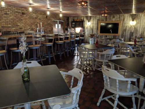 A rustic bar interior with wooden walls, high stools, and tables, featuring dim lighting and a cozy atmosphere.