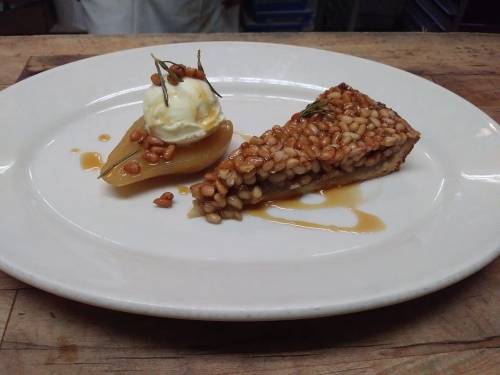 A slice of nut tart with caramelized pears and a scoop of vanilla ice cream, garnished with pine nuts.