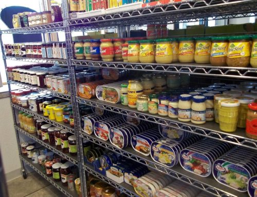 A well-organized pantry shelf filled with various jars and cans of sauces, spreads, and condiments.
