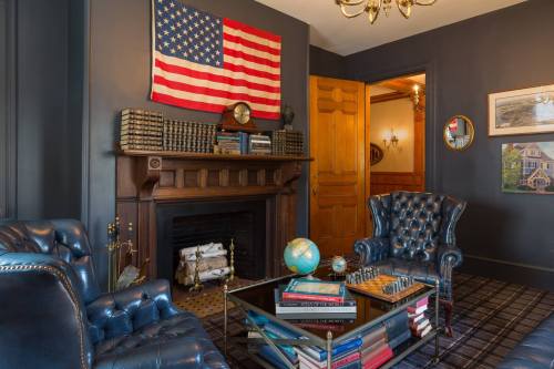 A cozy room with blue leather chairs, a fireplace, a globe, and an American flag on the wall.