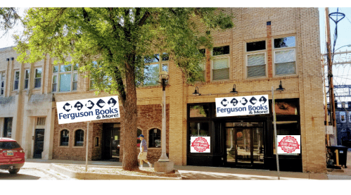 Exterior of Ferguson Books & More, featuring large signs, a tree, and a person walking by on a sunny day.