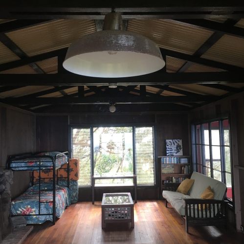 Cozy interior of a cabin with a bunk bed, sofa, coffee table, and large windows showcasing a natural view.