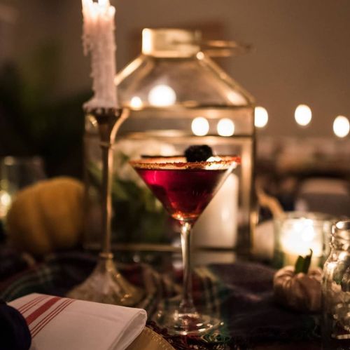 A beautifully set table with a cocktail, candlelight, and decorative elements, creating a cozy, festive atmosphere.