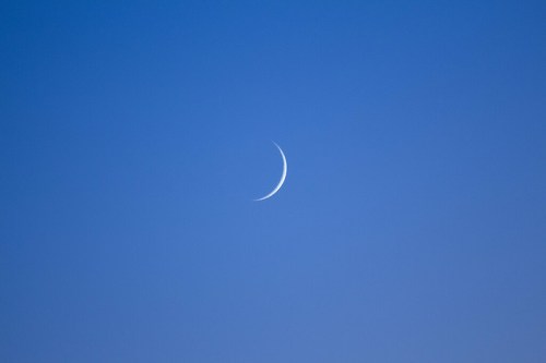 A thin crescent moon against a clear blue sky.