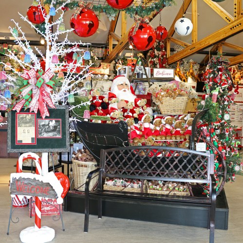 A festive display featuring Santa in a sleigh surrounded by teddy bears, holiday decorations, and a welcoming sign.