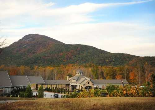A scenic view of a stone building surrounded by colorful autumn trees and a mountain in the background under a blue sky.
