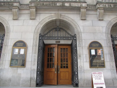 Entrance of a historic library building with wooden doors and decorative stonework, featuring informational plaques.