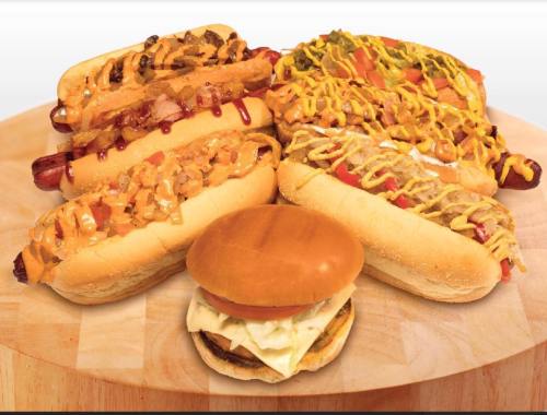 A wooden platter featuring various hot dogs topped with condiments and a burger with lettuce and tomato.