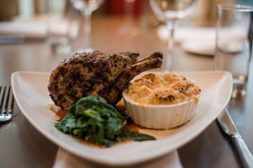 A plate featuring a seasoned pork chop, creamy casserole, and sautéed spinach, elegantly presented on a table.