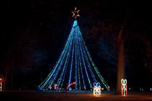 A brightly lit Christmas tree made of blue and green lights, topped with a star, surrounded by festive decorations.