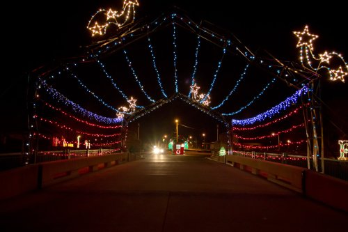 A brightly lit bridge at night, adorned with colorful holiday lights in red, blue, and white, creating a festive atmosphere.