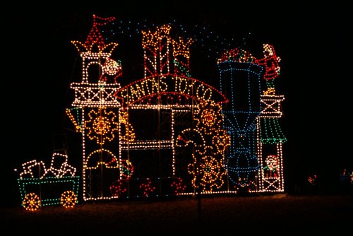 Colorful holiday lights form a festive display featuring a whimsical train and buildings against a dark night sky.