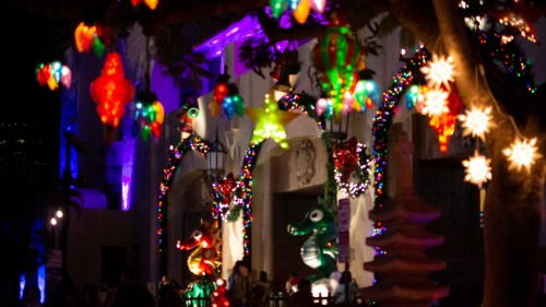 Colorful holiday lights and decorations illuminate a festive scene at night, with vibrant ornaments and glowing figures.