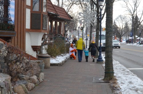 A costumed character greets a family on a snowy street lined with festive decorations and shops.