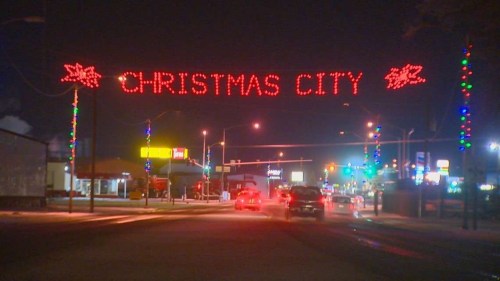 A festive street scene at night with a large "CHRISTMAS CITY" sign illuminated in red lights above the road.
