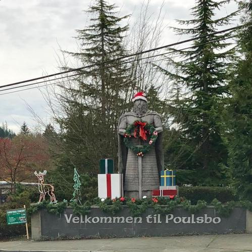 A large statue adorned with a Santa hat and holiday decorations, welcoming visitors to Poulsbo, surrounded by trees.