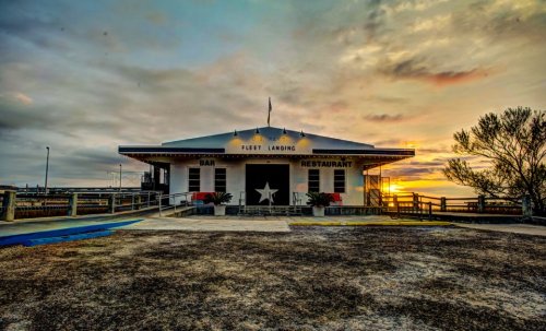 A waterfront restaurant with a star emblem, set against a colorful sunset and cloudy sky.