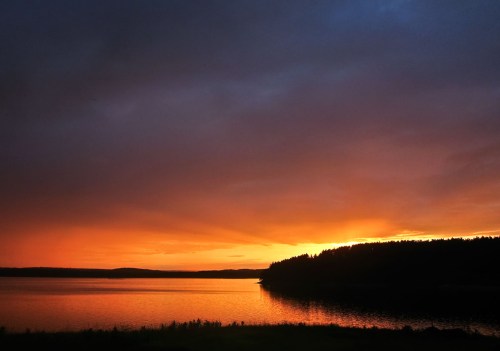 A serene sunset over a calm lake, with vibrant orange and purple hues reflecting on the water's surface.