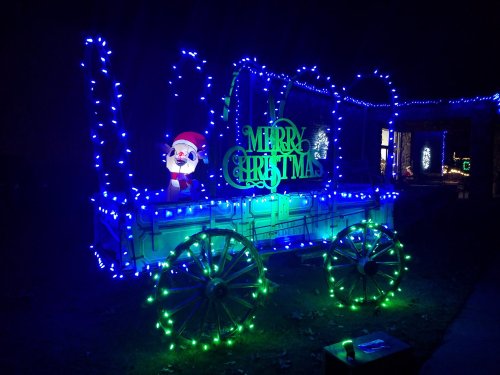 A festive display featuring a decorated wagon with blue and green lights, a Santa figure, and a "Merry Christmas" sign.