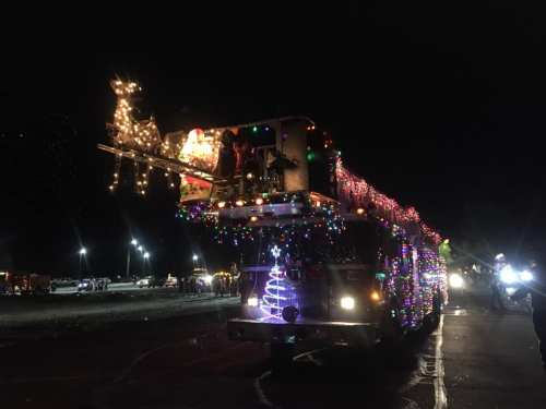 A festive truck adorned with colorful lights and decorations, featuring a reindeer and sleigh on top, at night.
