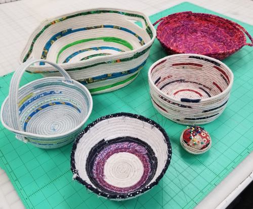 A collection of colorful, handmade fabric baskets of various sizes on a green cutting mat.