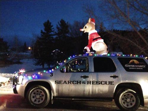 A decorated search and rescue vehicle with a large reindeer in a Santa outfit on the roof, set against a twilight backdrop.