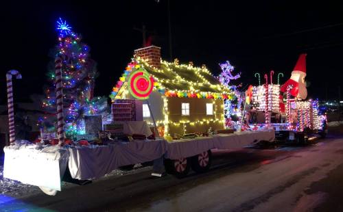 A festive parade float decorated as a gingerbread house with colorful lights, candy canes, and a large Santa figure.