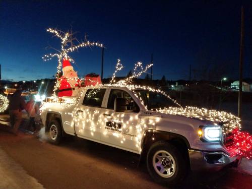 A decorated pickup truck with Christmas lights and a Santa figure, parked on a street at dusk.